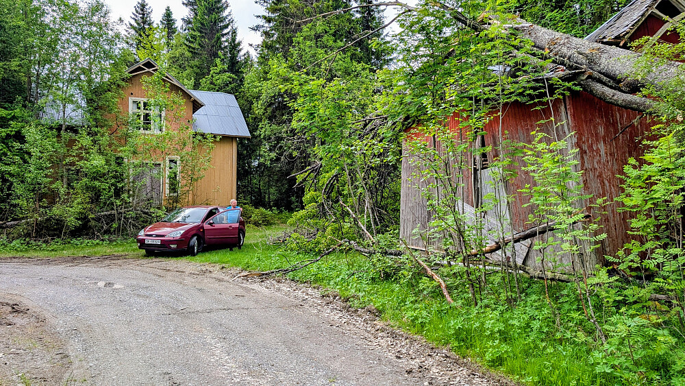 Parkering ved en falleferdig gammel skolebygning og en ruin av en annen bygning.