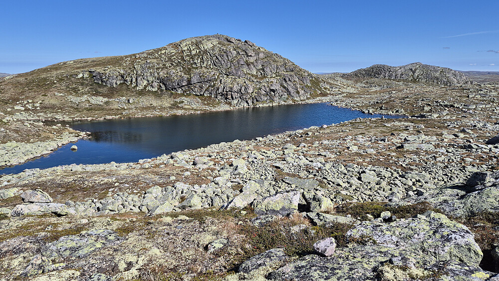 På andre siden av tjernet er toppen Vest for Torshalltjønni (1428). En fin liten tind fra denne kanten, og synlig varde på toppen. Til høyre ses den lavere Sørvest for Torshalltjønni (1416).