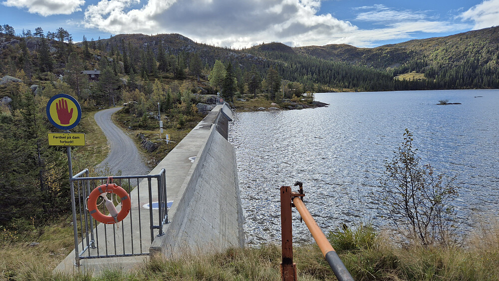 Demningen jeg gikk forbi. Bak til venstre ses bilen min delvis bak noen busker. Nærmest er bommen som kun hadde en pinne som lås.